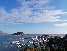 Marina Budva panorama, with many yachts berthed inside. Behind it, island is St. Nicholas is visible. Old town of Budva is on the right, next to the Marina.